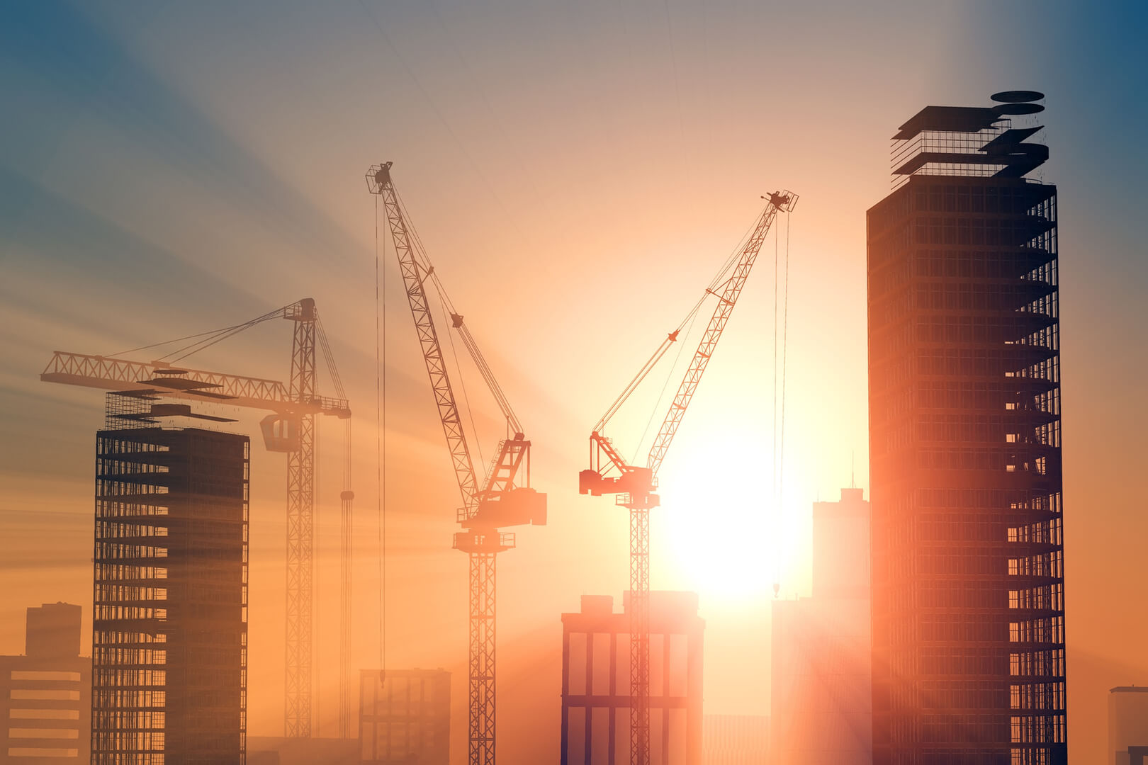 Construction cranes building skyscrapers at sunset.
